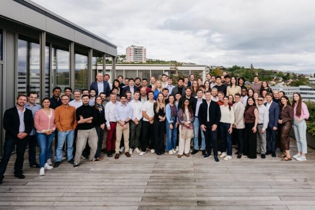 Large diverse group of professionals posing on a rooftop deck for a team photo.