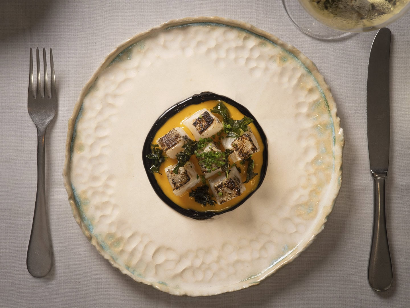 Small black bowl with orange sauce and grilled tofu cubes garnished with greens, centered on a textured plate.