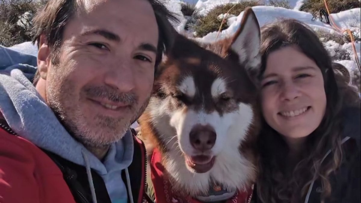 Couple posing with a happy husky dog in a snowy outdoor setting.