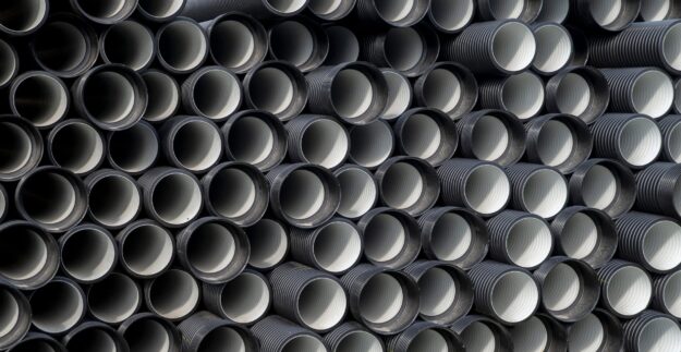 Stacked black corrugated plastic pipes viewed from the end, showing ridged interiors and circular openings.