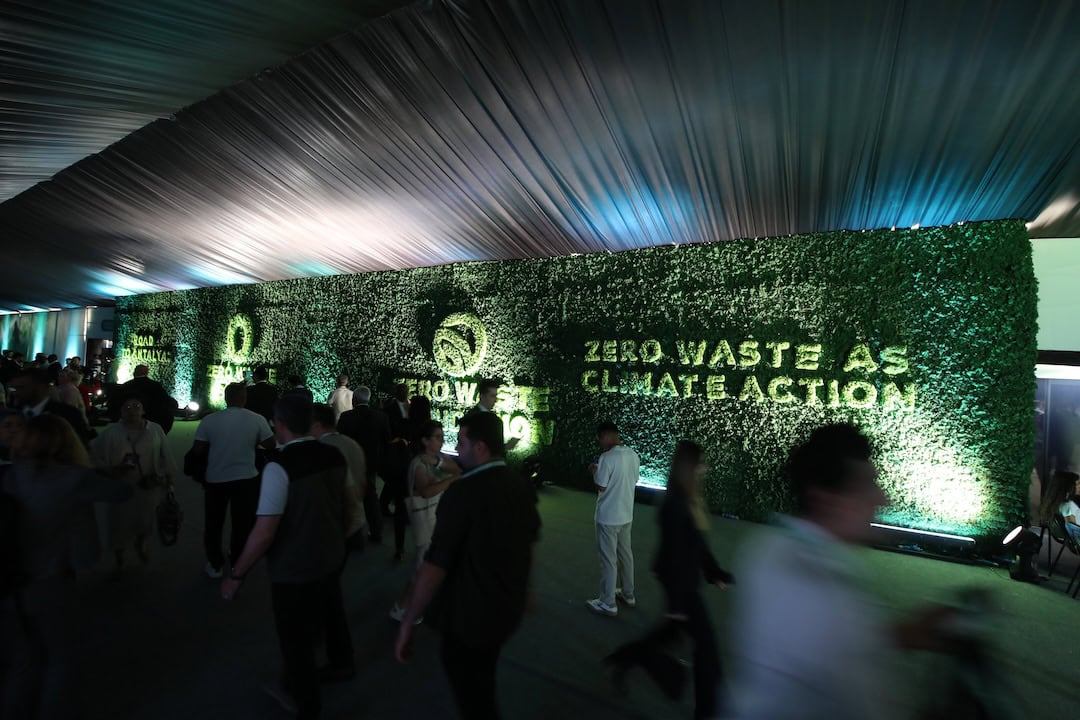 Indoor event with a green hedge wall that reads 'Zero Waste Climate Action' while attendees walk by.