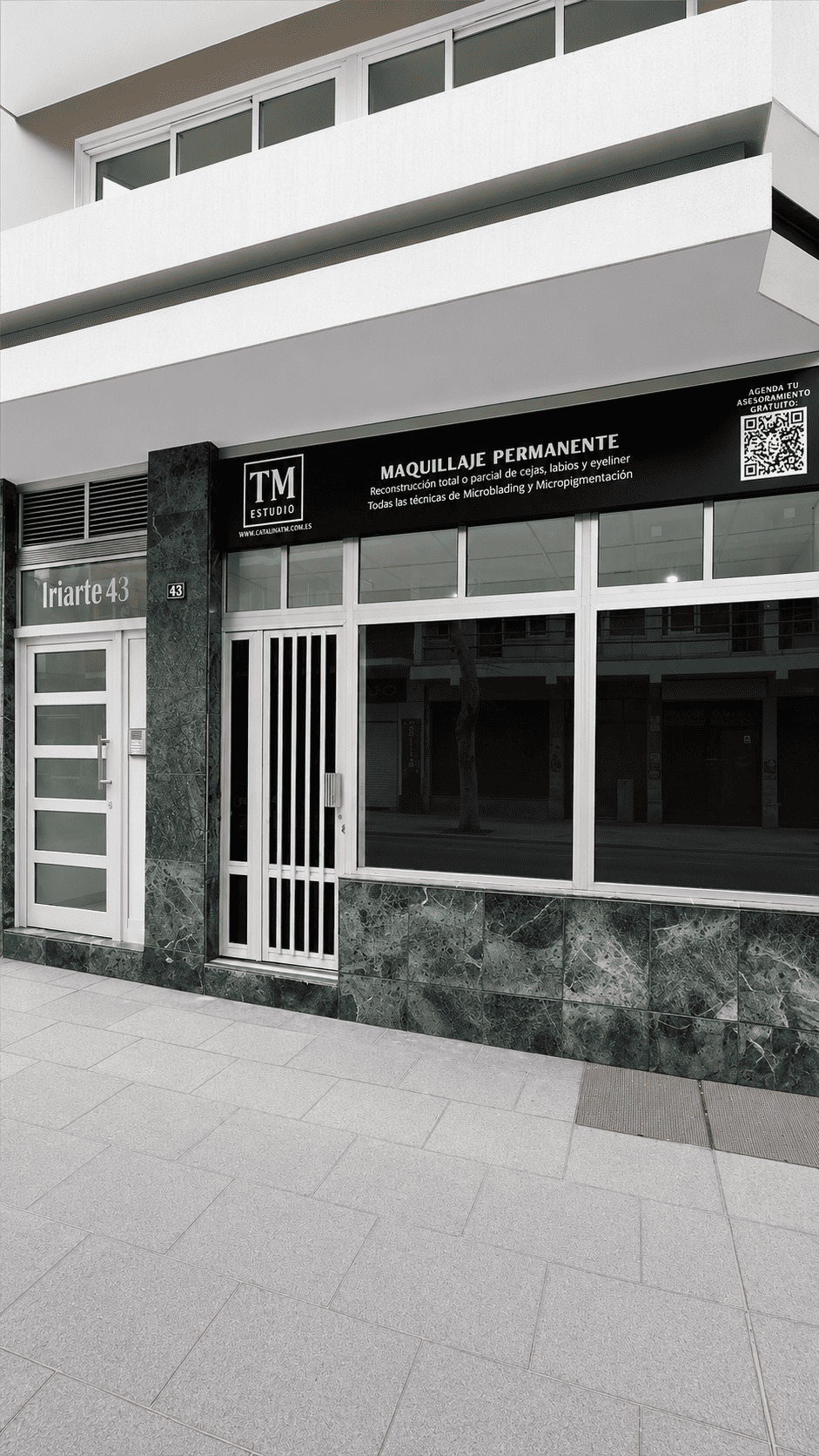 Storefront of a beauty studio with a black sign reading 'MAQUILLAJE PERMANENTE' above large glass windows and marble facade, urban sidewalk outside