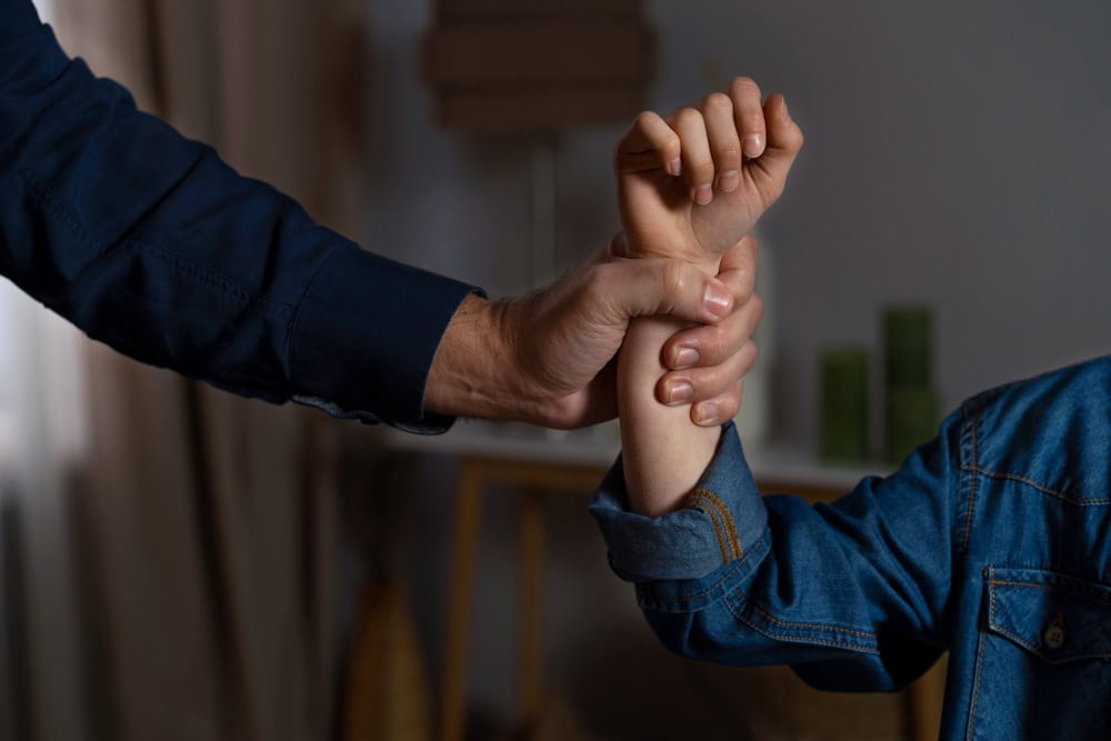 Adult hand firmly holding a child's forearm in a home setting, suggesting guidance or safety support.