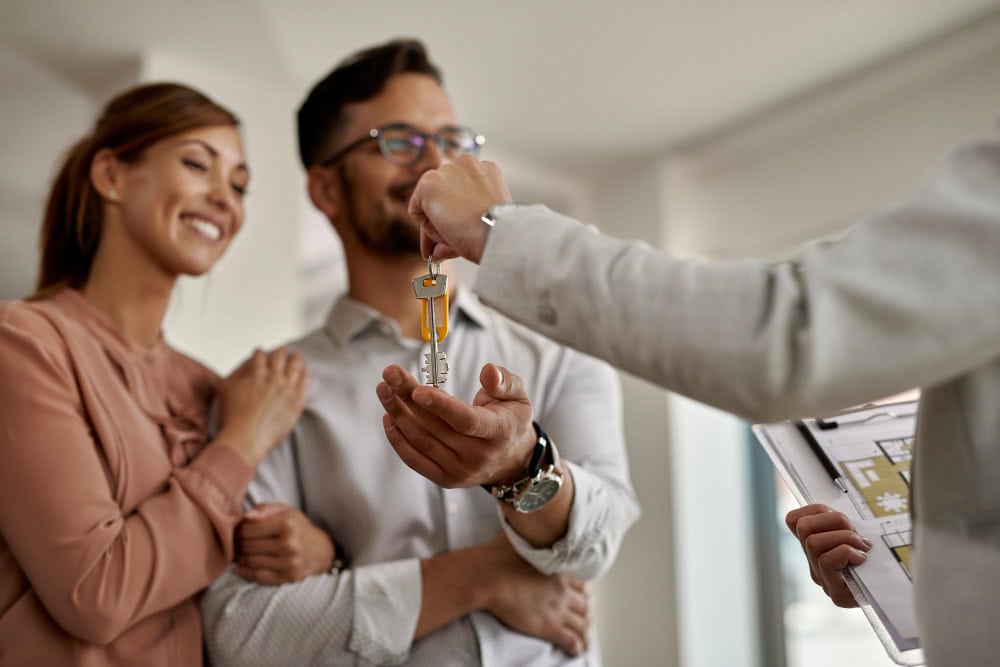 Happy couple receiving house keys from a real estate agent, celebrating a new home.