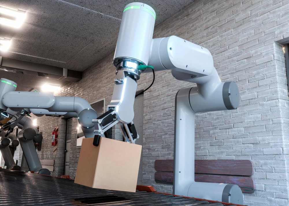 Industrial robotic arm lifting a cardboard box onto a conveyor belt in a brick-walled facility with bright overhead lights.