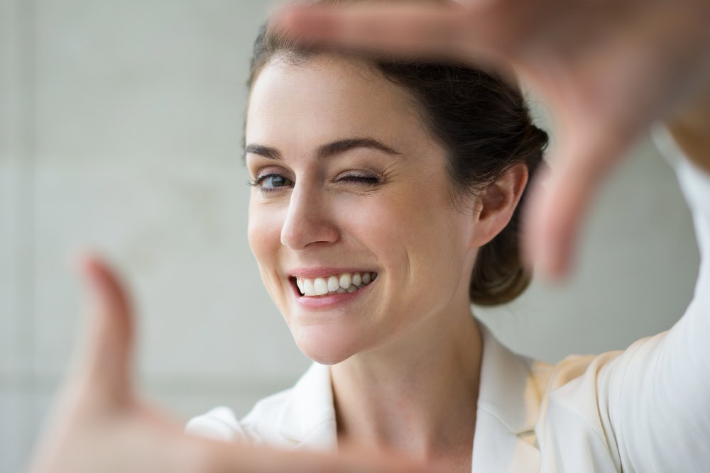 Smiling woman winking at the camera while taking a selfie, with hands framing the shot.