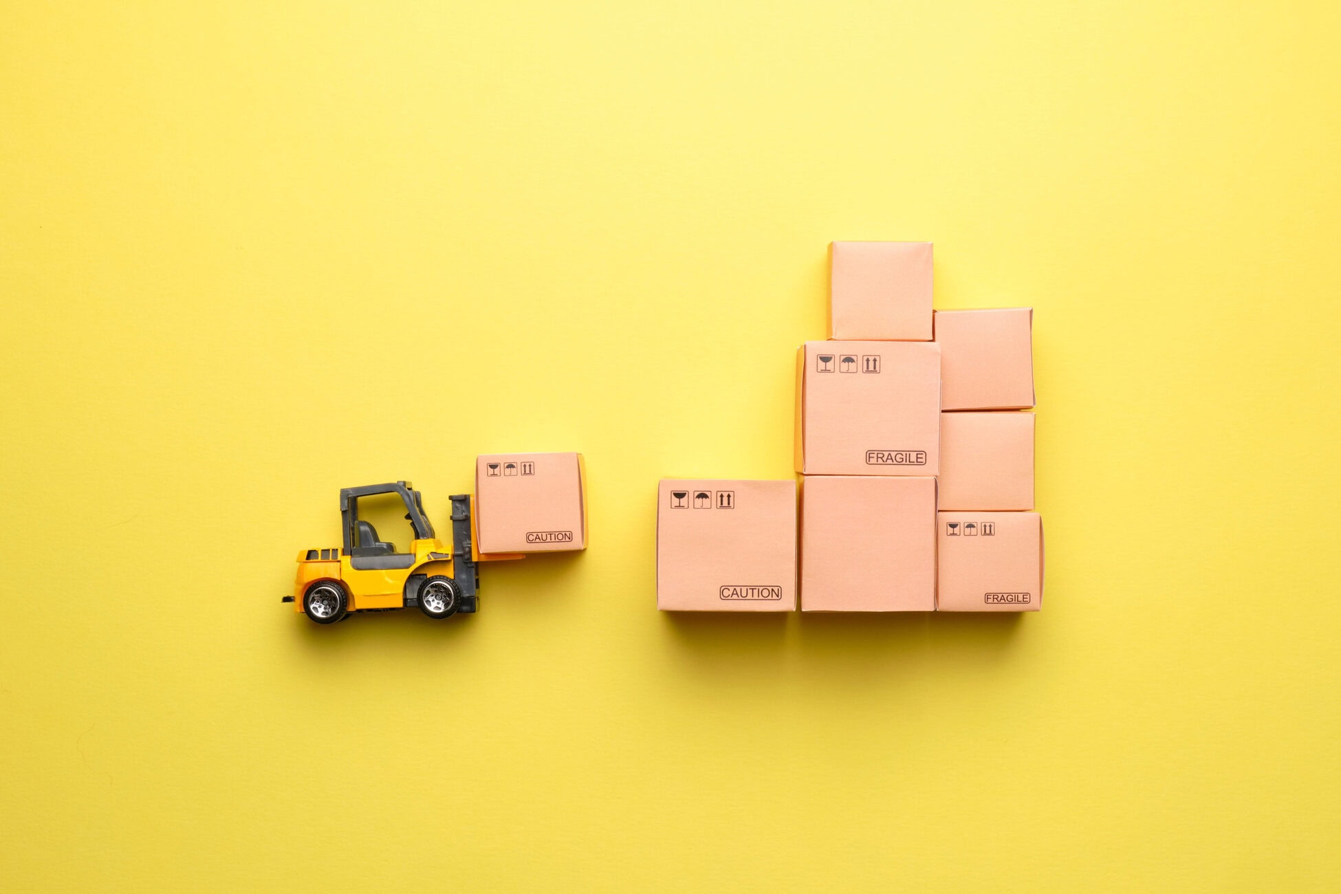 Toy forklift moving a fragile box stack against a bright yellow background.
