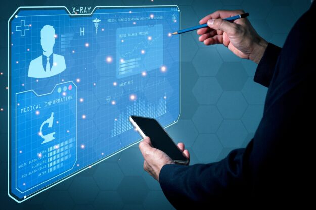 Hands interact with a blue holographic medical dashboard while holding a smartphone nearby on a dark suit sleeve