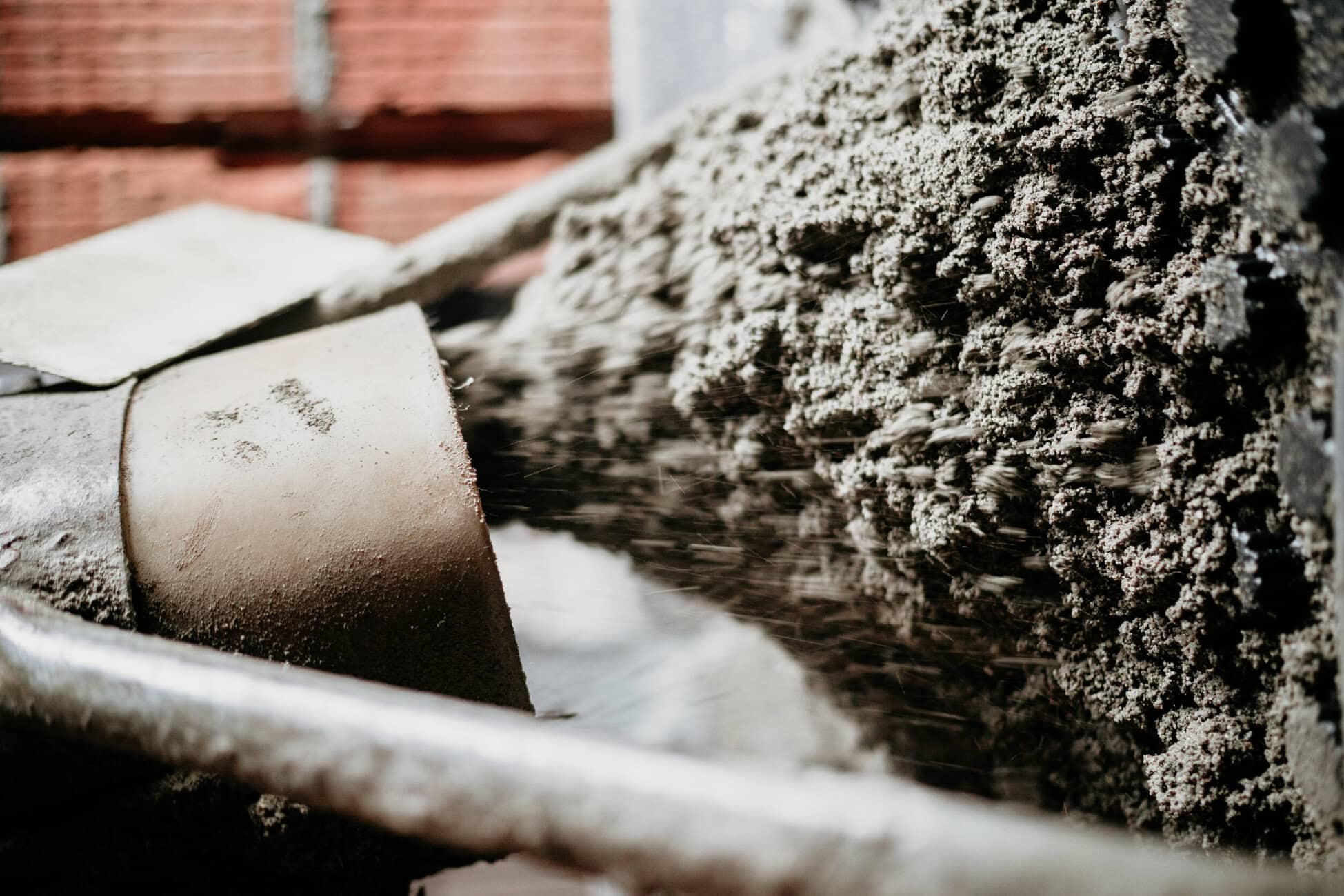 Close-up of a construction site with a pile of wet concrete mix beside stacked concrete blocks and a brick wall in the background.