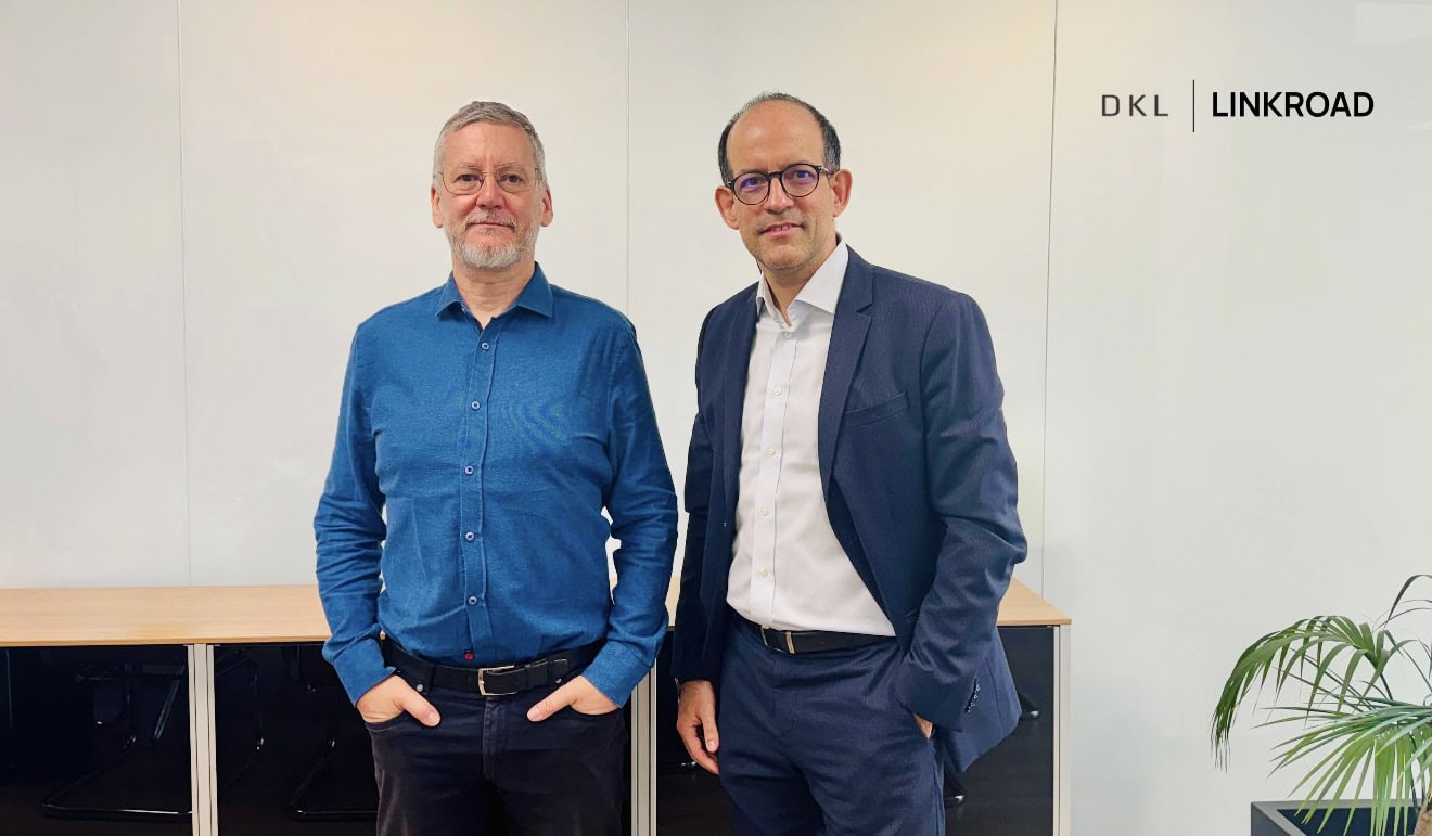 Two colleagues pose in a bright office; left man in blue shirt, right man in navy suit, with DKL LINKROAD logo on the wall behind them.