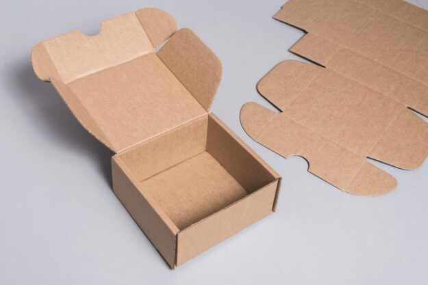 Open brown cardboard box with flaps spread, plus flat die-cut templates on a gray surface.
