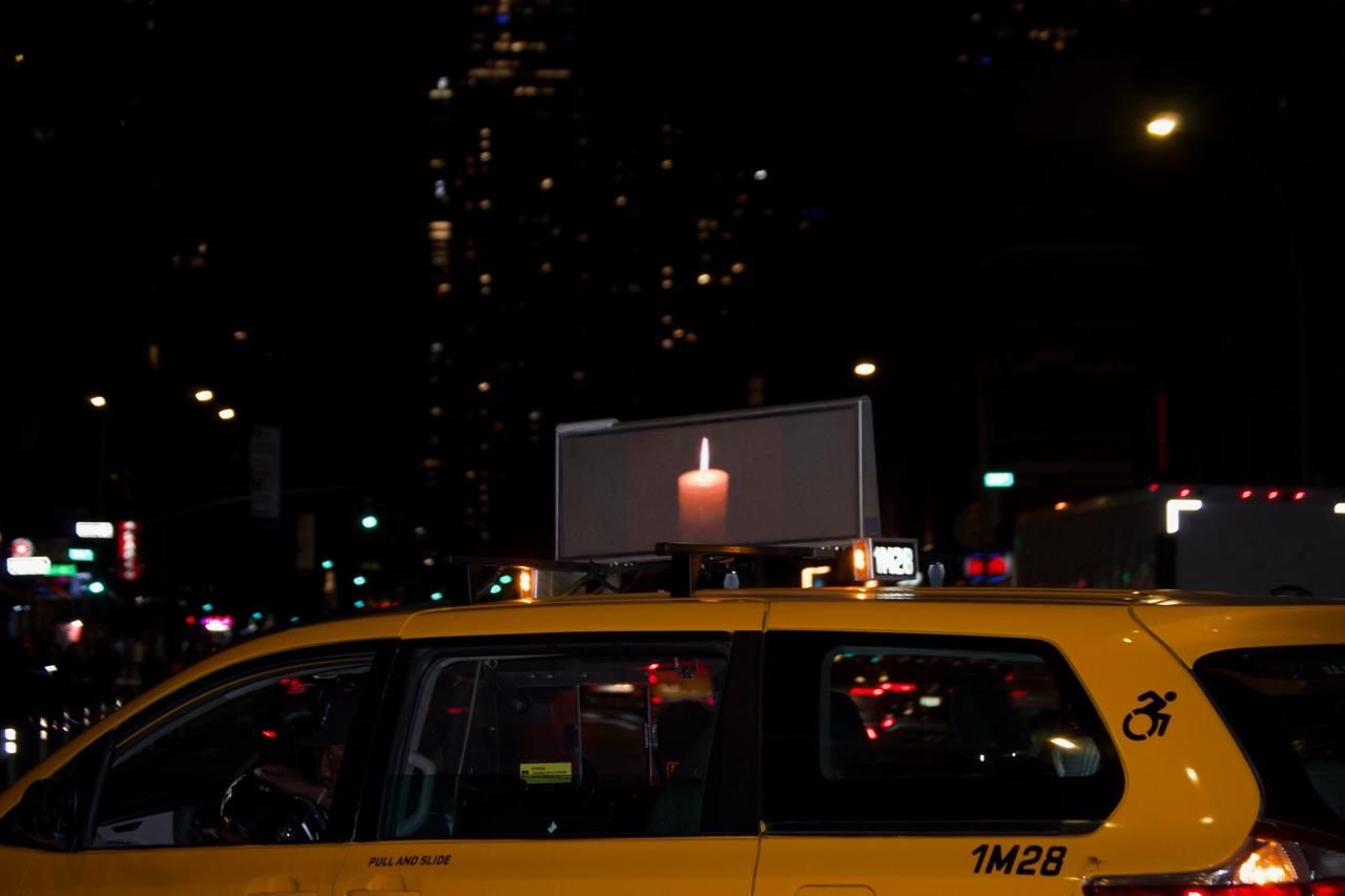 Yellow taxi at night with a rooftop billboard displaying a lit candle against a dark city street backdrop.