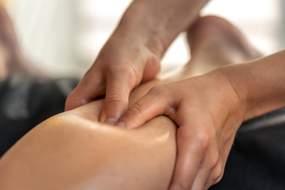 Therapist's hands massaging a person's leg, focusing on the calf near the knee.