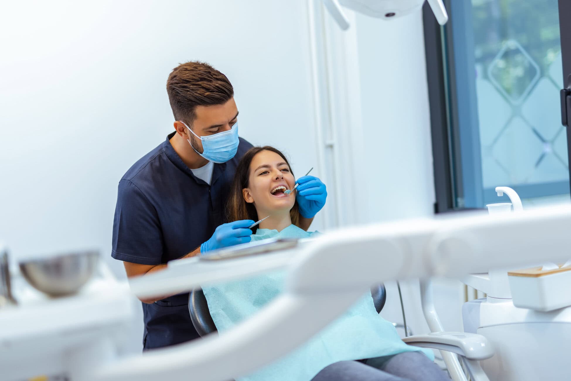 Dentist wearing a mask and gloves treating a patient in a bright dental clinic.