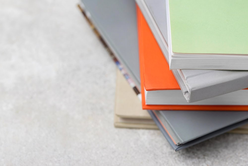 Stack of colorful hardcover notebooks stacked on a gray surface, with orange, gray, beige, and green covers.