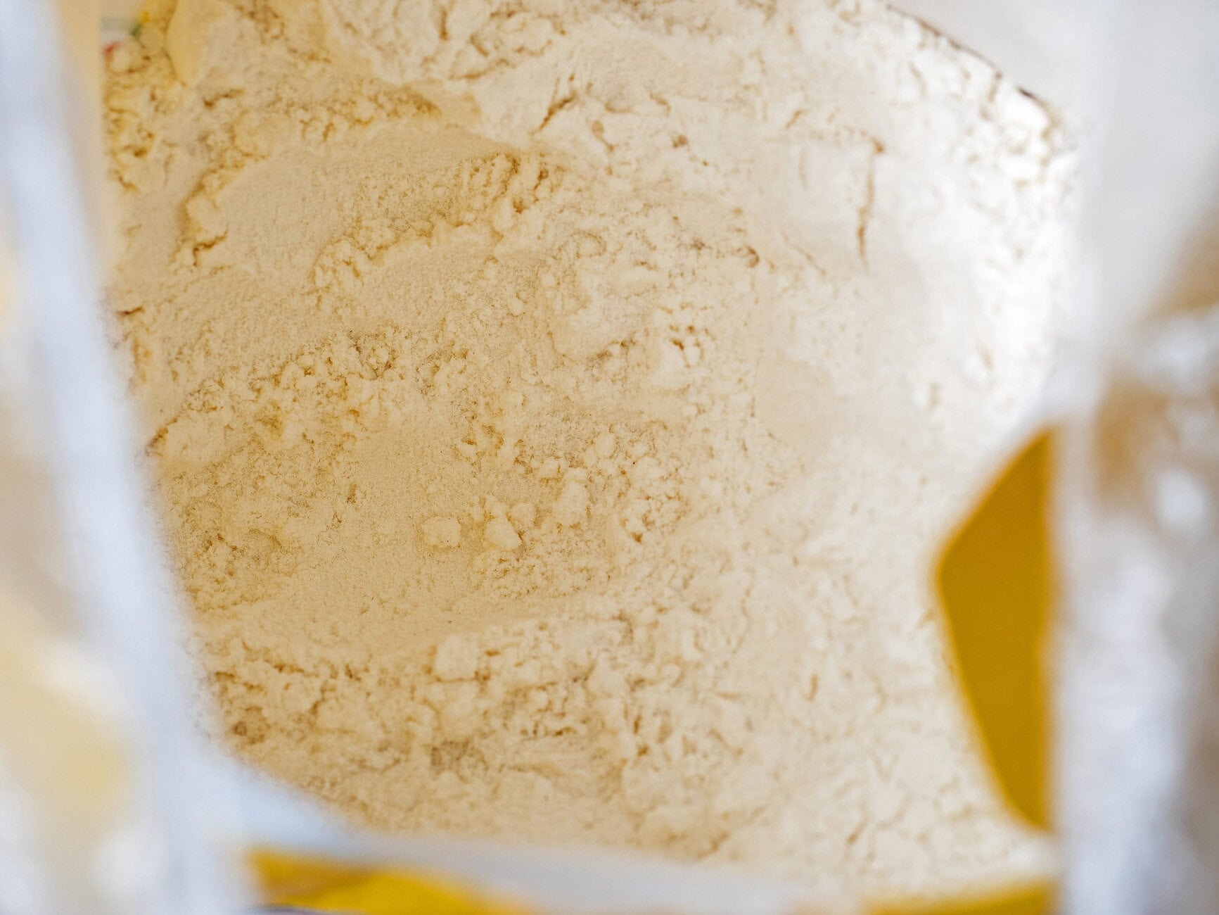 Close-up of light tan flour piled inside a white bag with yellow accents.