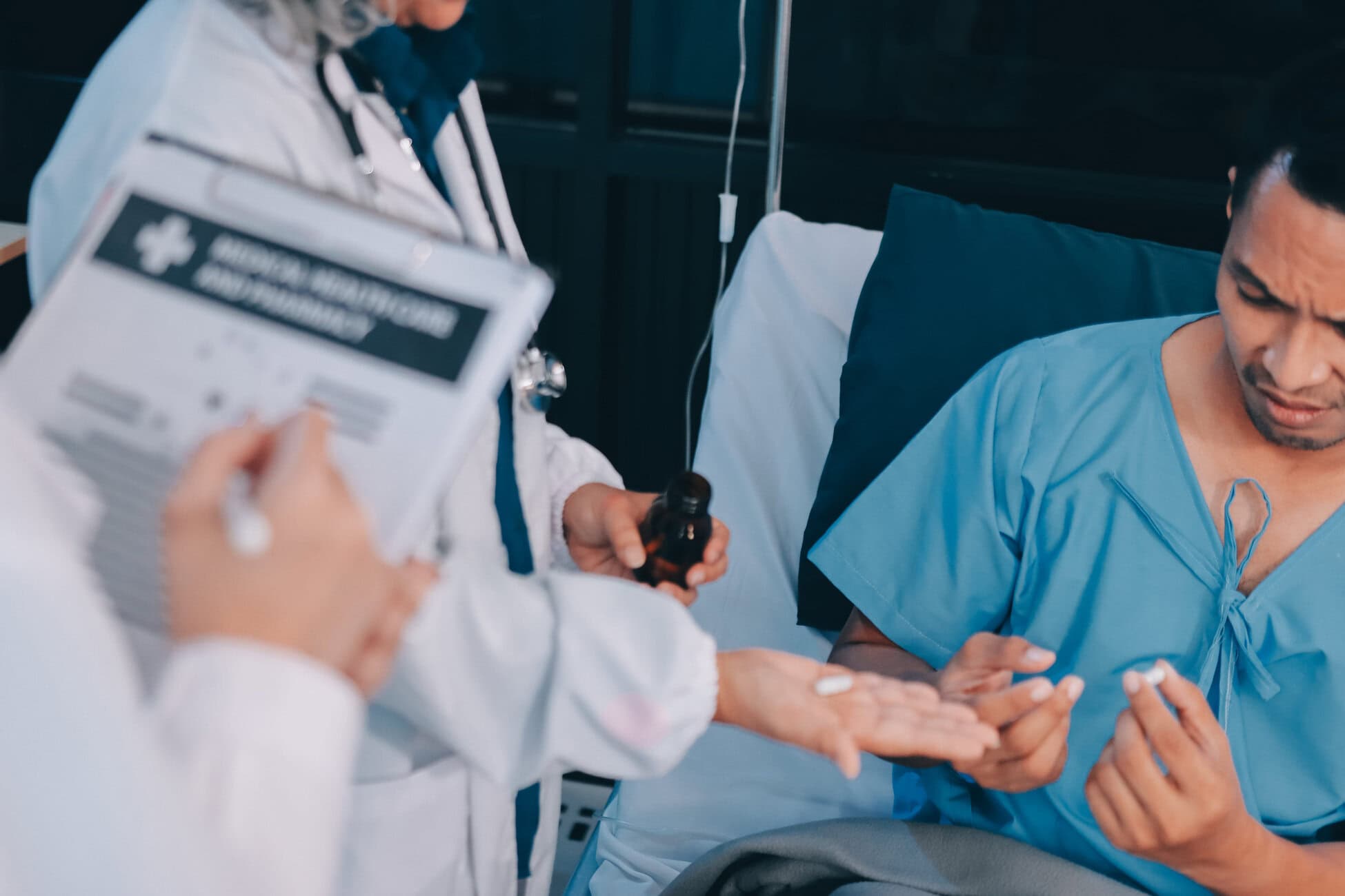 Nurse in a white coat and mask prepares medication for a patient seated in a hospital bed within a clinical setting.