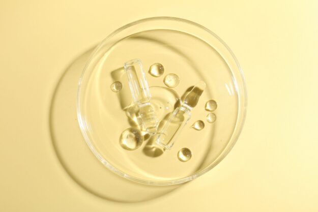 Top-down close-up of a glass bowl with ice cubes and droplets on a pale yellow surface.