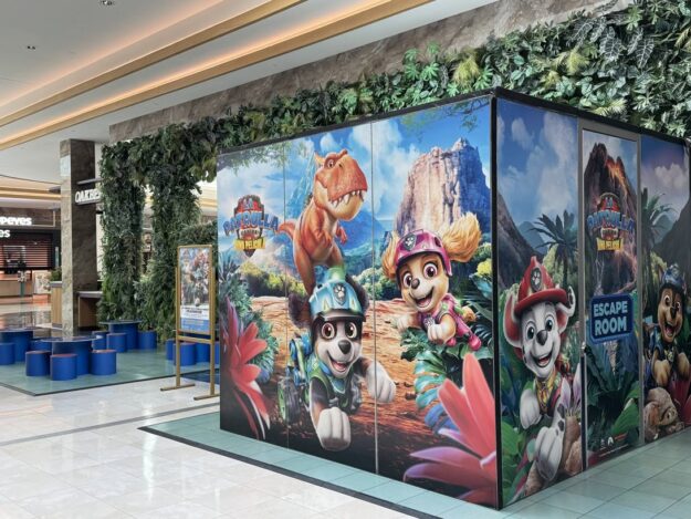 Paw Patrol-themed display panels in a shopping mall, featuring colorful characters against a jungle landscape with seating nearby.