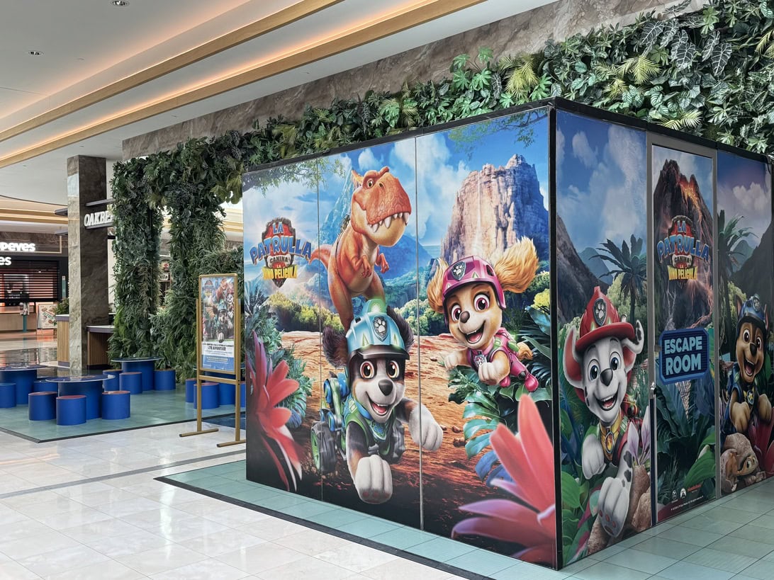 Paw Patrol-themed display panels in a shopping mall, featuring colorful characters against a jungle landscape with seating nearby.