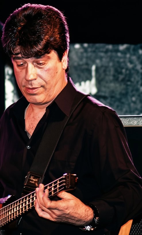 Male musician playing a bass guitar on stage, focused on the fretboard during a live performance