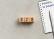 Wooden blocks spell 'B2B' beside a notebook page reading 'BUSINESS TO BUSINESS' with a silver pen nearby.