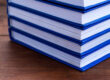 Stack of blue-bound hardcover books stacked on a wooden table surface.