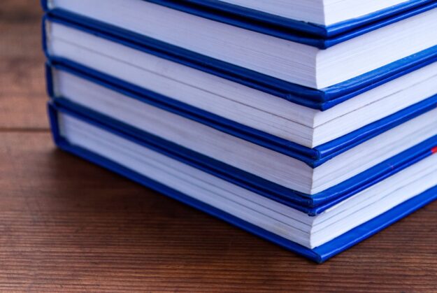 Stack of blue-bound hardcover books stacked on a wooden table surface.