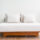 White cushioned outdoor sofa with two pillows on a wooden base, placed on a balcony next to a glass railing.”, “Minimalist white lounge sofa with beige cushions on a wooden platform against a light wall and sliding door.”, “Outdoor daybed with white cushions and a wooden frame on a balcony.”, “Two pillows rest on a white sofa on a wooden platform on a balcony with glass railing.”]}} )?Oops. Need proper JSON without quotes issues. Ensure valid JSON. Let's redo.```json ...``` Remove stray characters.```json{