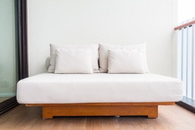 White cushioned outdoor sofa with two pillows on a wooden base, placed on a balcony next to a glass railing.”, “Minimalist white lounge sofa with beige cushions on a wooden platform against a light wall and sliding door.”, “Outdoor daybed with white cushions and a wooden frame on a balcony.”, “Two pillows rest on a white sofa on a wooden platform on a balcony with glass railing.”]}} )?Oops. Need proper JSON without quotes issues. Ensure valid JSON. Let's redo.```json ...``` Remove stray characters.```json{