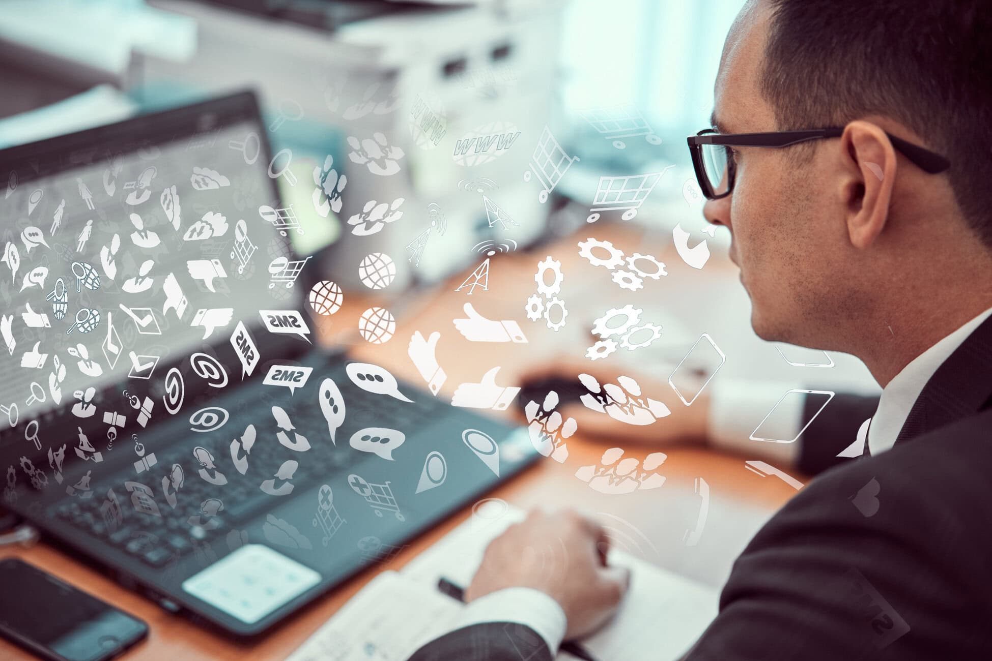 Businessman in a suit typing on a tablet at a desk with white digital icons overlaying the scene