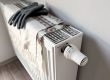 Radiator heater with a plaid blanket and gray knit gloves resting on top, indoors.