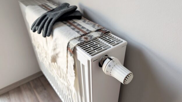 Radiator heater with a plaid blanket and gray knit gloves resting on top, indoors.