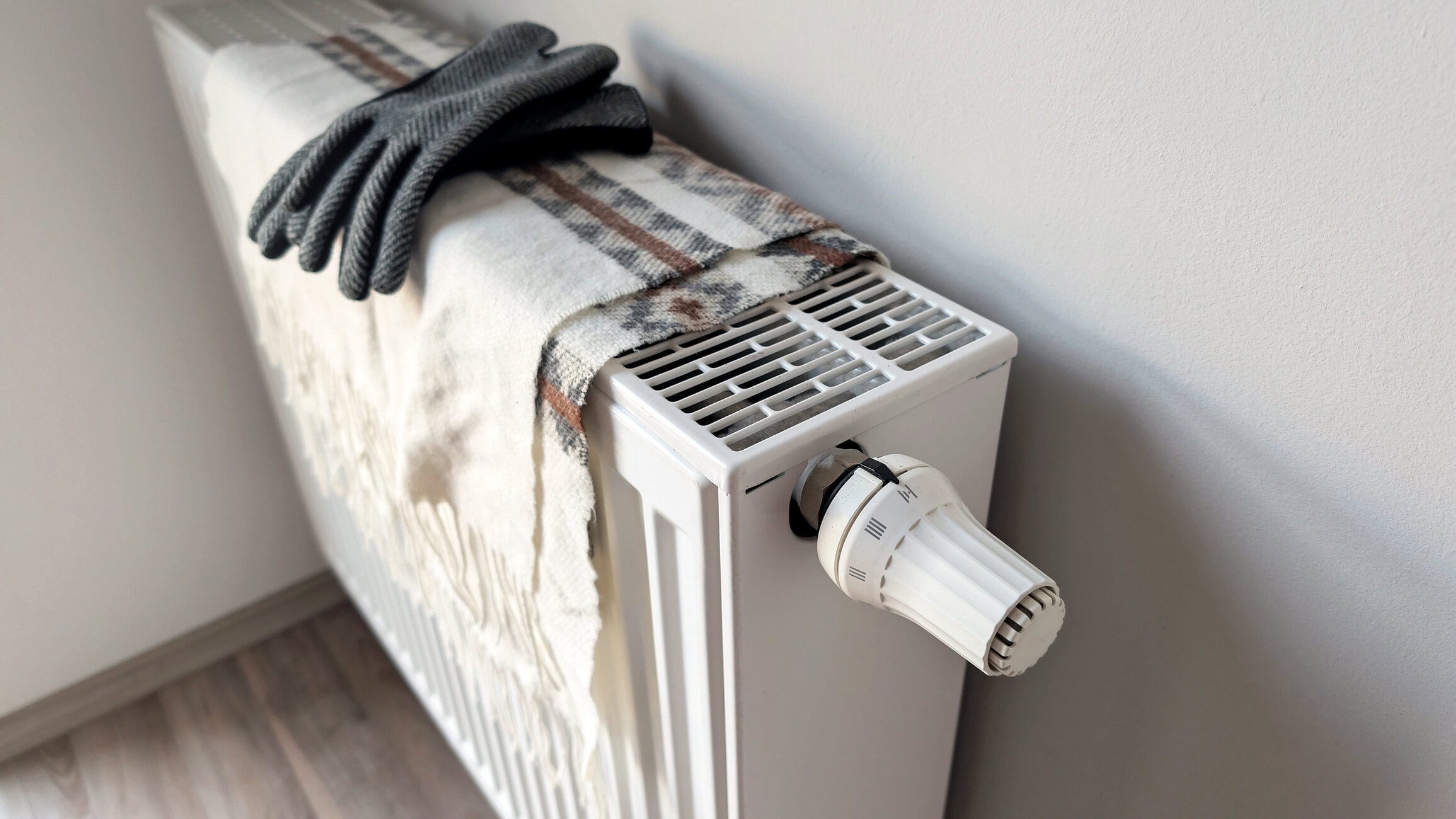 Radiator heater with a plaid blanket and gray knit gloves resting on top, indoors.