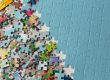 Colorful jigsaw pieces scattered across a surface beside a mostly completed blue puzzle center-right.