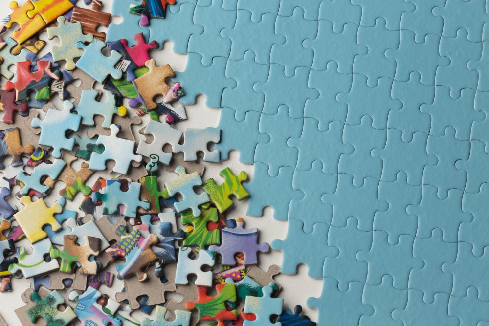 Colorful jigsaw pieces scattered across a surface beside a mostly completed blue puzzle center-right.