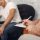 Therapist writing on a clipboard during a therapy session, while a man sits in the background with his hand on his head.