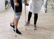 Person with a knee brace using crutches during physical therapy, with a clinician nearby for support.