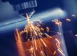 Close-up of a laser cutting machine emitting sparks as it cuts through metal in blue-toned lighting, showcasing the industrial process.