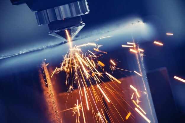 Close-up of a laser cutting machine emitting sparks as it cuts through metal in blue-toned lighting, showcasing the industrial process.