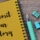 Yellow spiral notebook reading 'Submit Your Story' beside a teal pen and binder clips on a wooden desk.