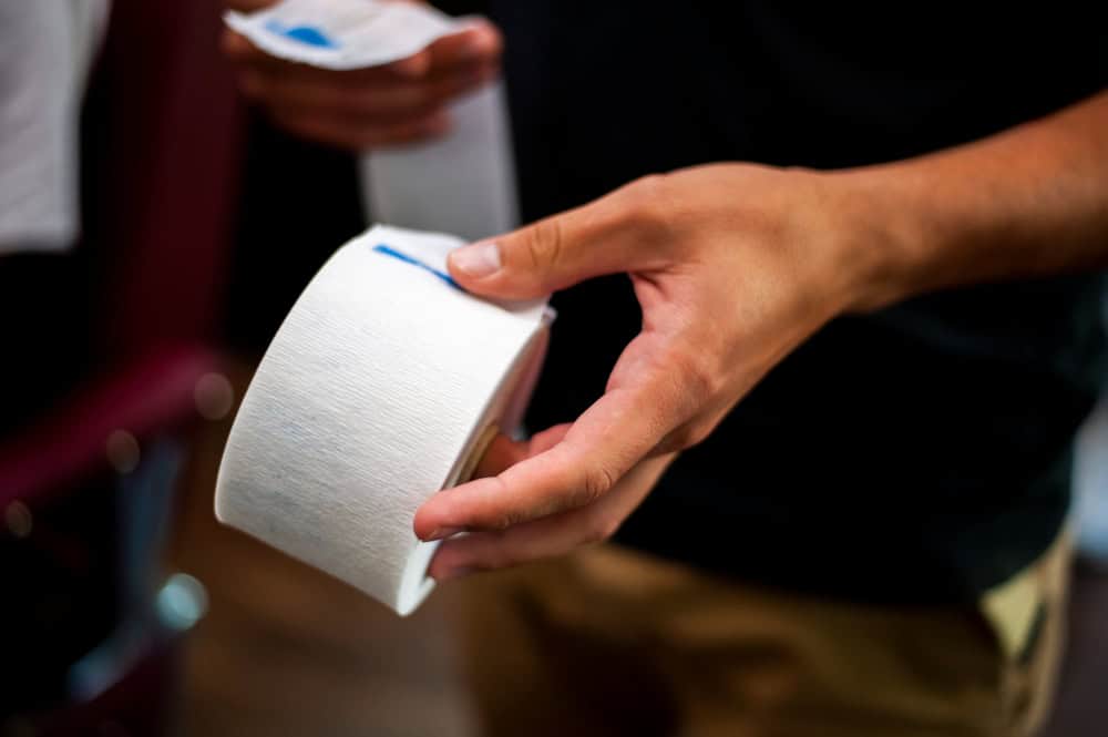 Close-up of a hand tearing off a sheet from a white roll of tissue or toilet paper.