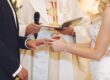 Bride and groom exchange rings during a wedding ceremony, with a clergy member holding a book in the background