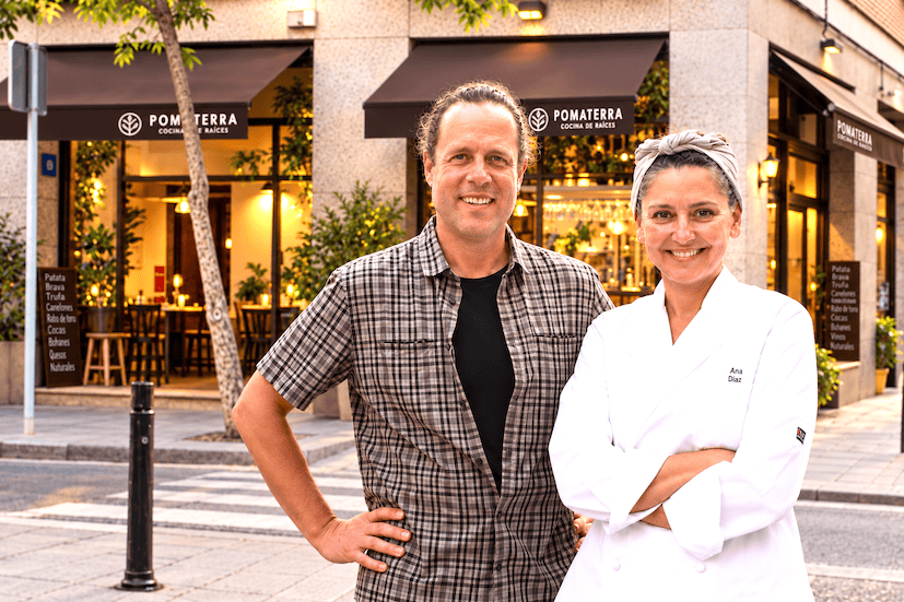 Chef Ana Diaz and a man in a plaid shirt pose outside Pomaterra restaurant on a sunny street.