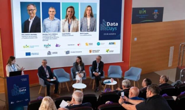 Panel discussion at Data Days with four speakers on stage and a large screen showing portraits and logos behind them.