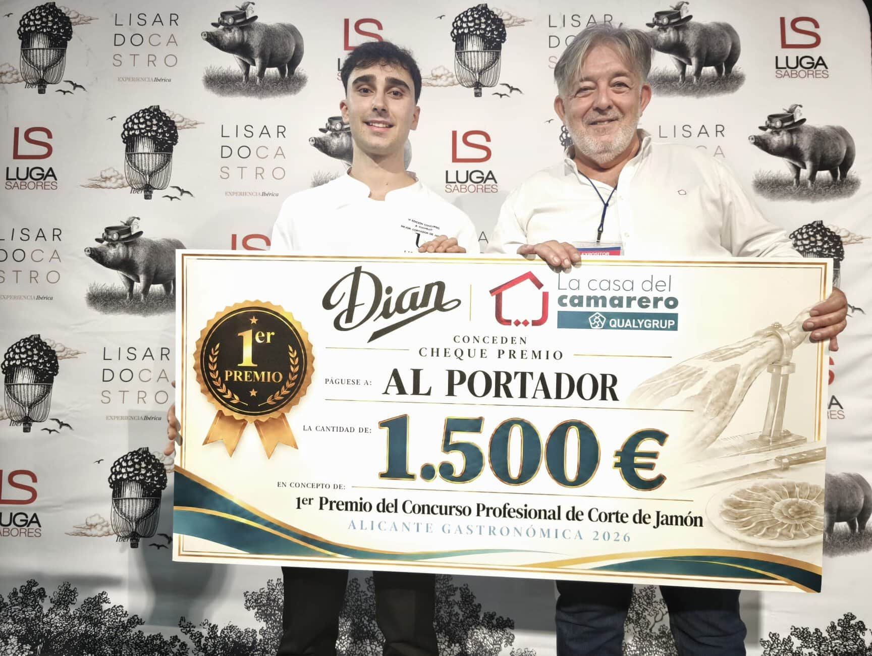 Two men pose with a giant cheque for 1,500 €, winning a ham-cutting contest, in front of sponsor banners with pig illustrations.