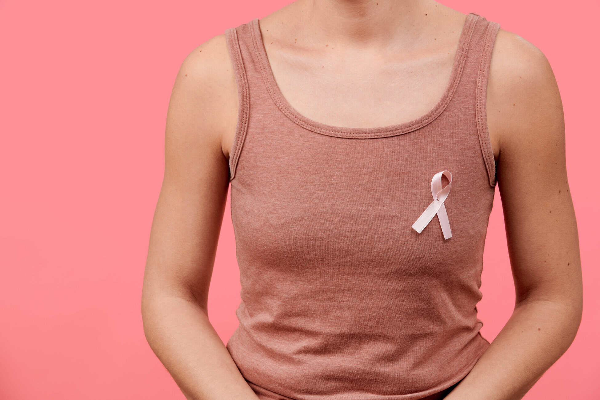 Partial view of a person wearing a pink tank top with a pink breast cancer awareness ribbon on the chest, against a pink background.