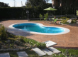 Kidney-shaped in-ground pool in a brick patio, with a green umbrella table set and surrounding garden.