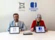 Two people sit at a round white table with tablets showing Shams and ORIGO Studios logos, against a light wall with the same logos behind them, a man in a gray blazer and a woman in red.