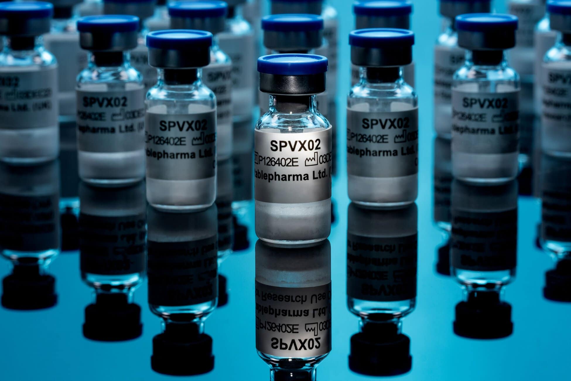 Row of small glass vials with blue caps labeled SPVX02 in a laboratory setting on a reflective surface.